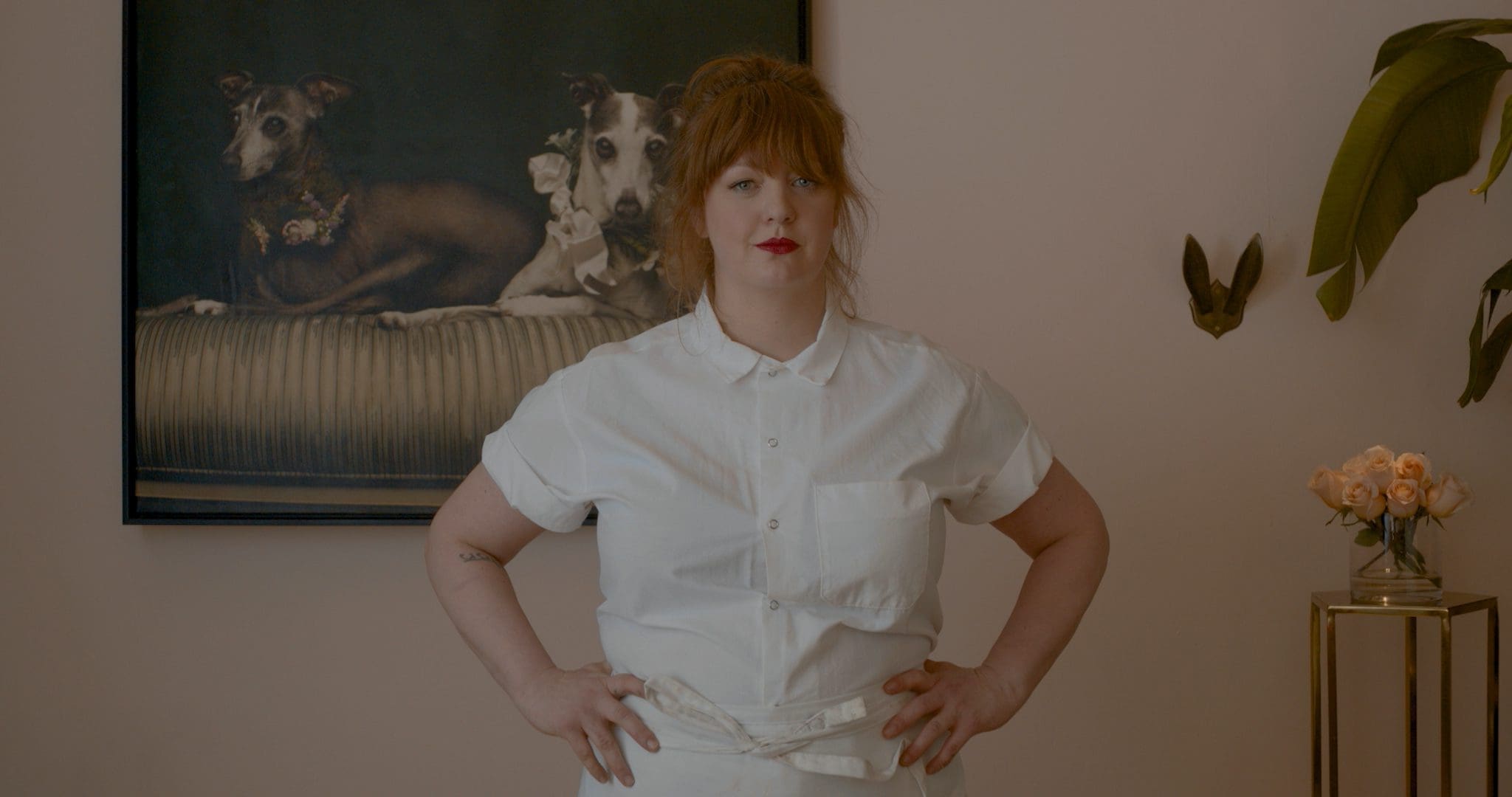 Chef Jamie Malone standing in front of a framed portrait of her beloved dogs, showcasing her connection to home and her personal life.