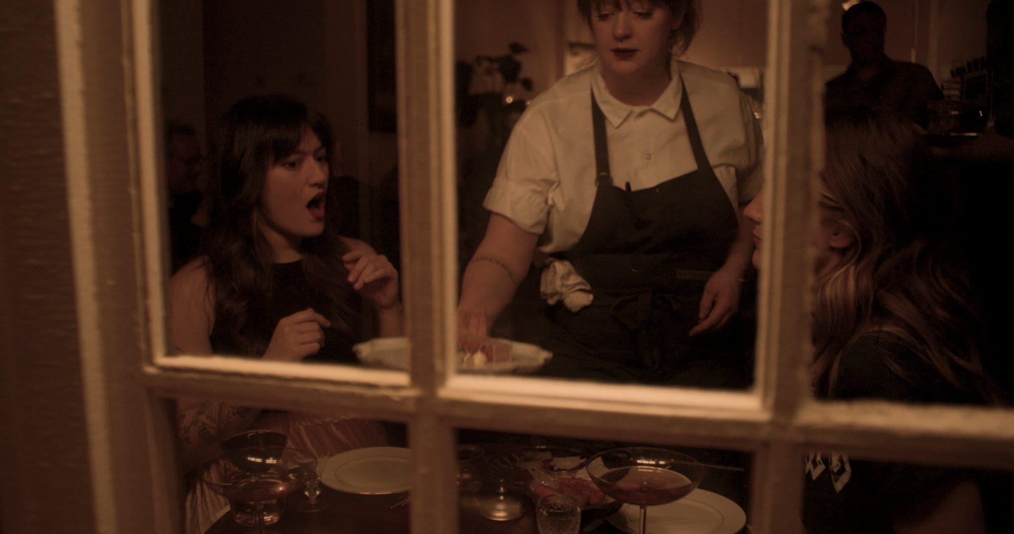 Chef Jamie Malone serves food to guests at Grand Cafe, captured through a window, highlighting the intimate and welcoming atmosphere of the restaurant.