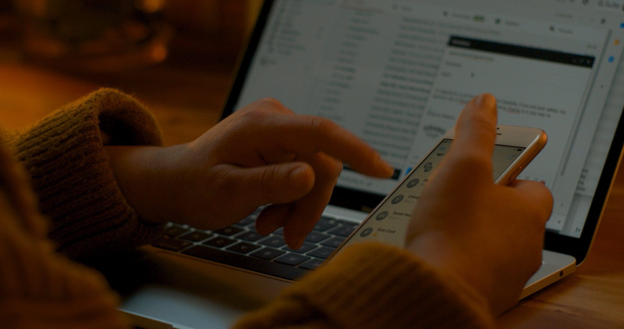 Close-up of Jamie Malone working in a cozy home office, using a laptop and smartphone, showcasing multitasking and a warm, productive space.