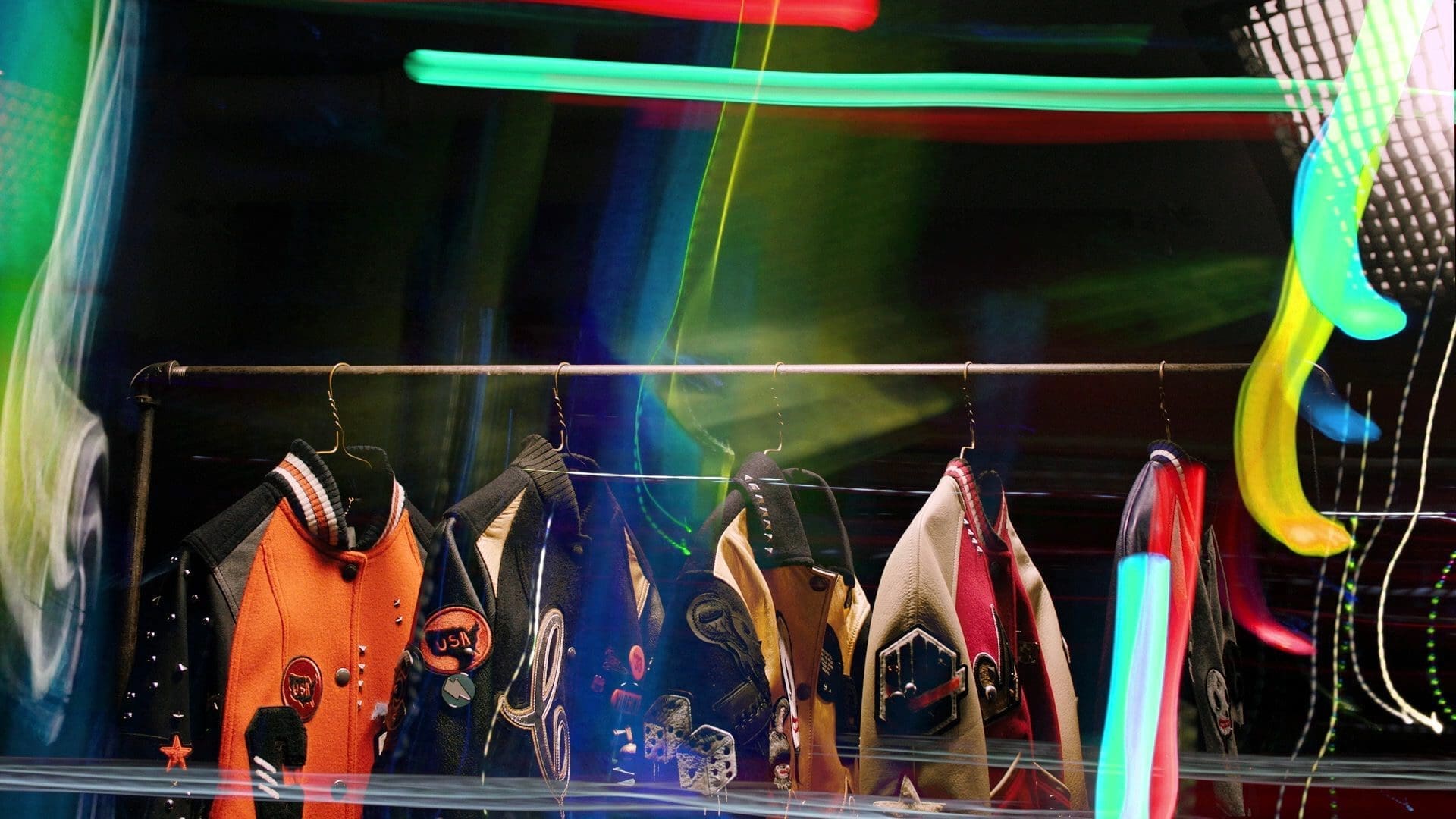 Coach Varsity jackets from the Women’s Fall 2016 collection displayed on a rack with neon graffiti-inspired lighting effects.