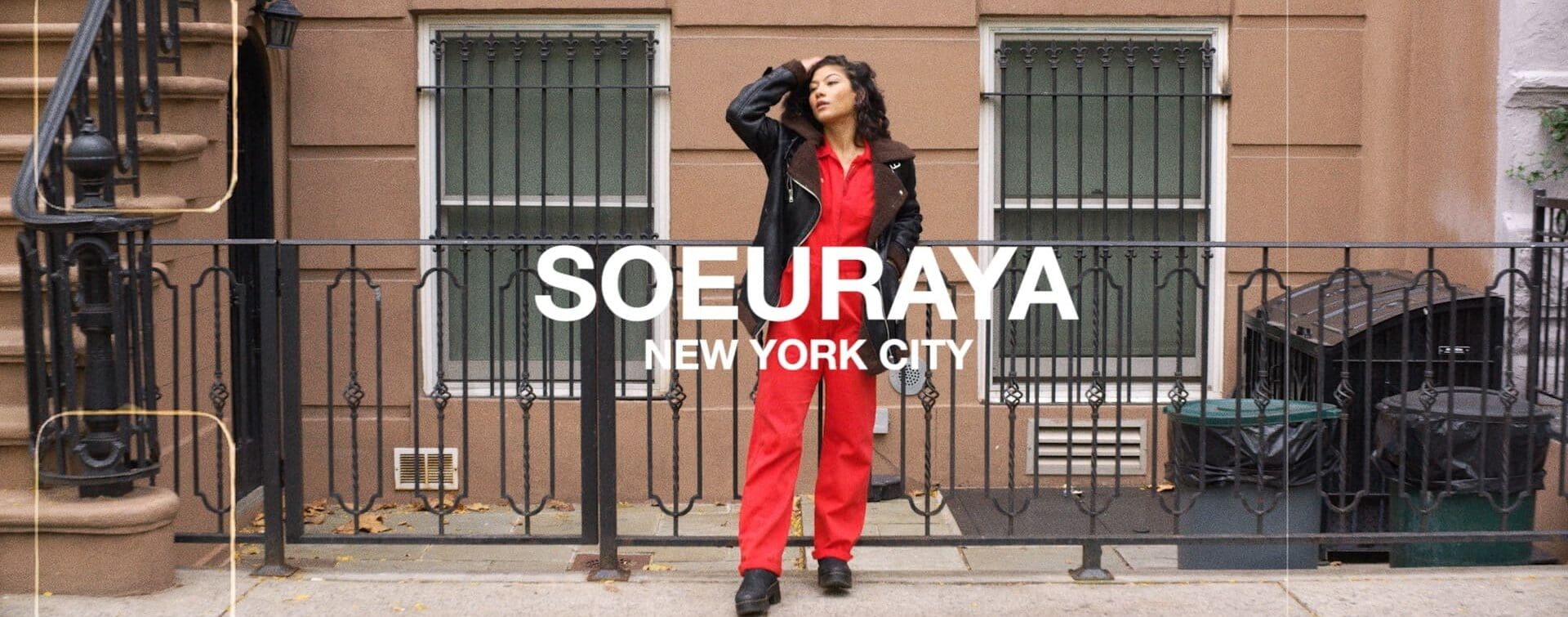 SoulCycle Docufilm_ Souereya00001 Soureya, poised and stylish in red jumpsuit and black jacket, stands confidently on a New York City street, embodying the urban energy and personal empowerment central to the SoulCycle Docufilm narrative
