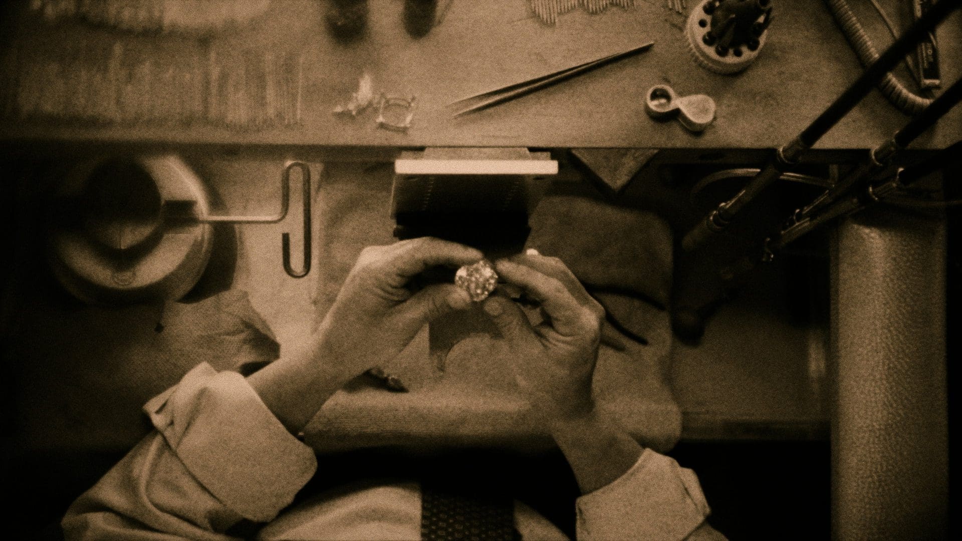 RIOT, NYC Creative Agency: Sepia-toned photo of a Tiffany & Co. jeweler meticulously inspecting a diamond ring, highlighting the intricate craftsmanship in a workshop setting. Sepia-toned photo of a Tiffany & Co. jeweler meticulously inspecting a diamond ring, highlighting the intricate craftsmanship in a workshop setting.