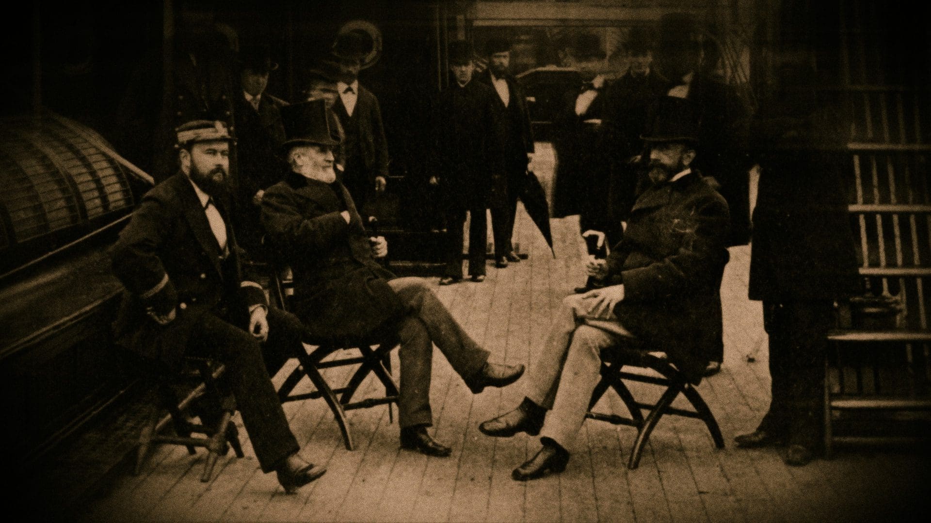 RIOT, NYC Creative Agency: Sepia-toned historical photograph capturing Charles Lewis Tiffany and group of gentlemen in period attire, including top hats and suits, engaged in conversation while seated on folding chairs, likely depicting a scene from the late 19th or early 20th century. Sepia-toned historical photograph capturing Charles Lewis Tiffany and group of gentlemen in period attire, including top hats and suits, engaged in conversation while seated on folding chairs, likely depicting a scene from the late 19th or early 20th century.