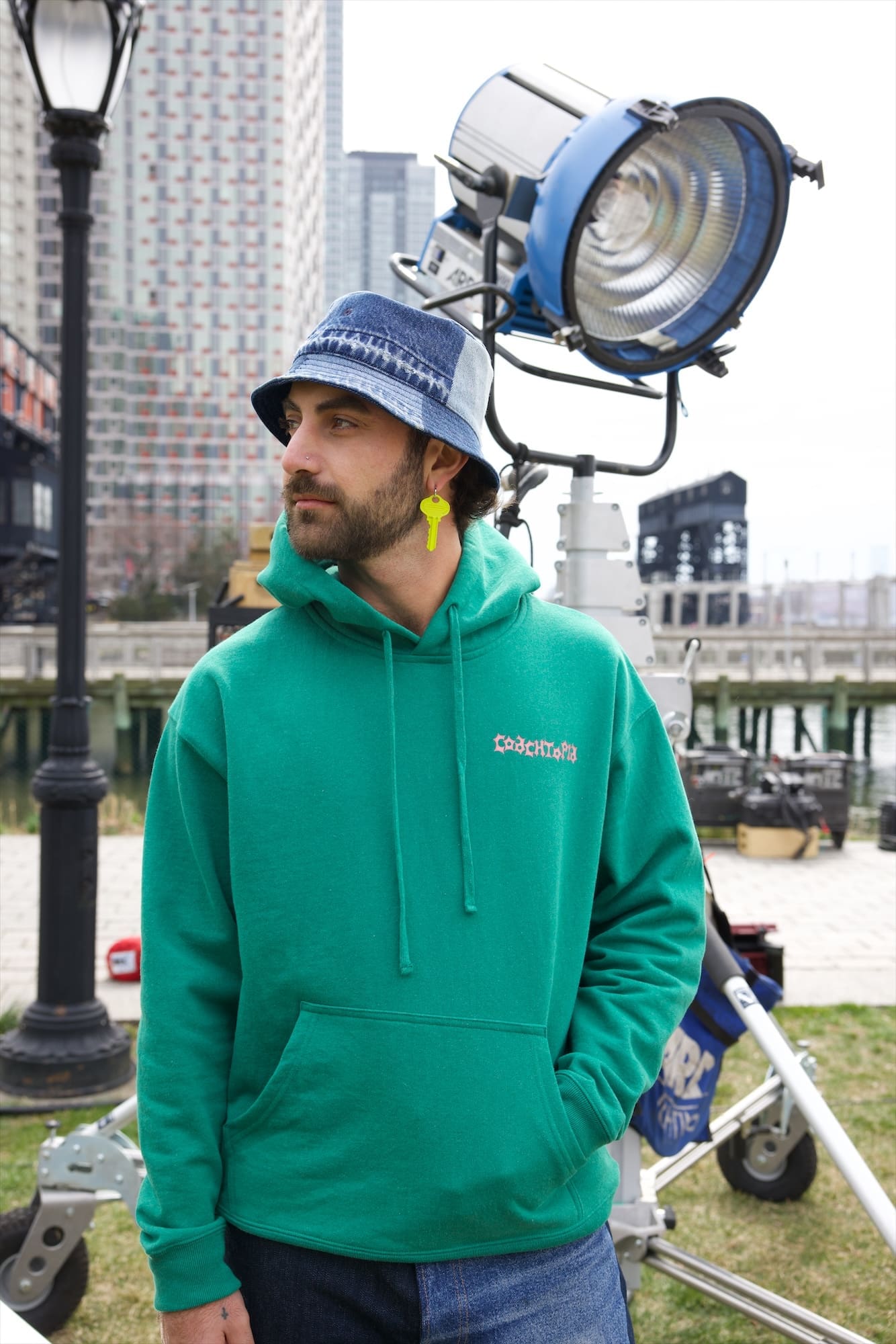 Caulin in a denim bucket hat and green Coachtopia hoodie beside a film light