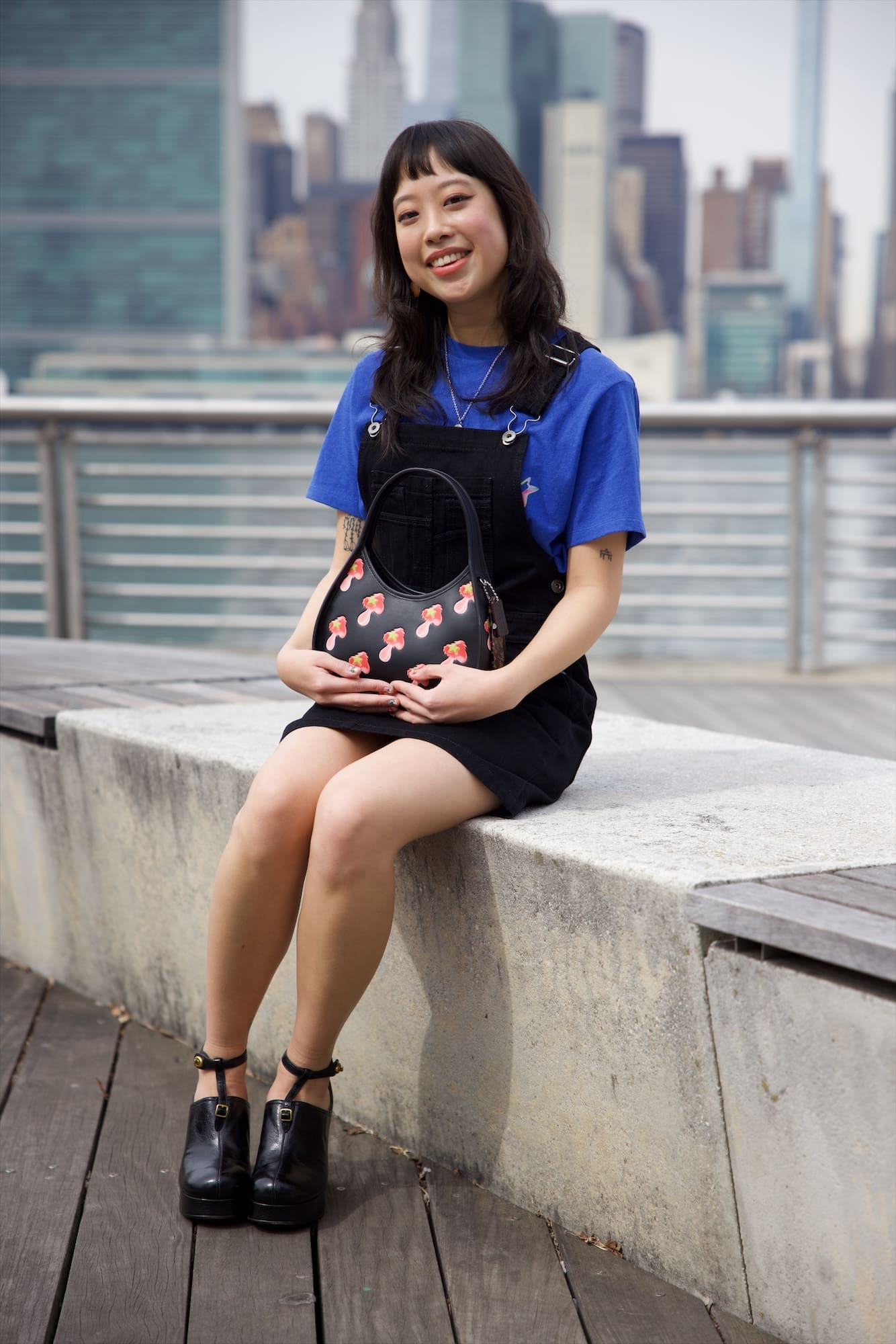 Sabrina Lau sitting on the waterfront wall with the Manhattan skyline behind
