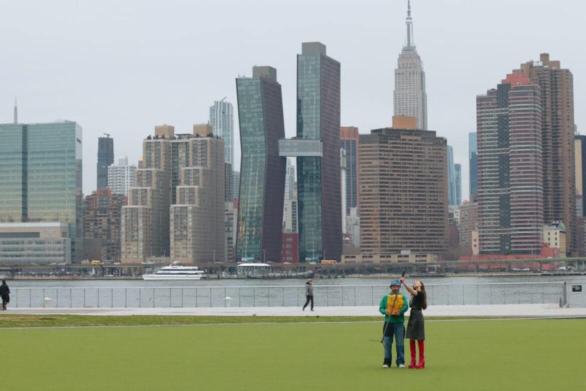 Two Coachtopians on the lawn at Gantry Plaza State Park with the Manhattan skyline across the river