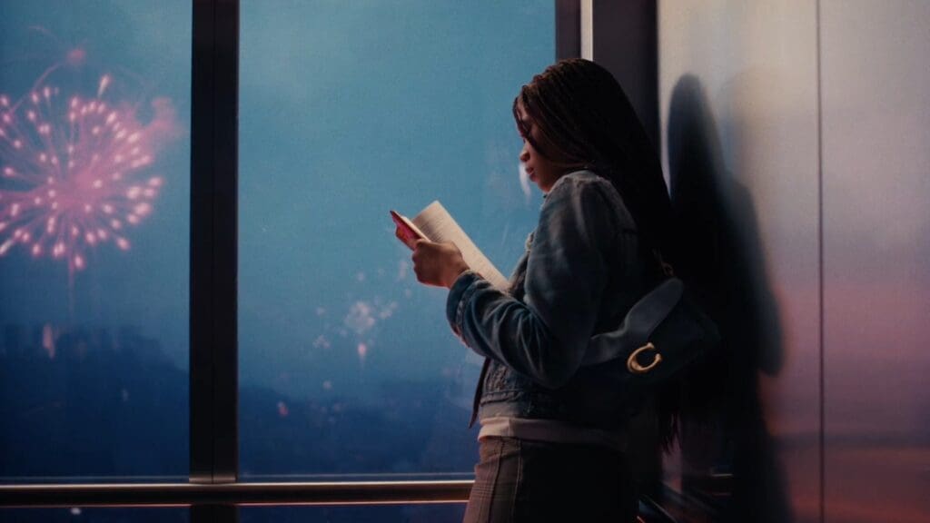 A woman reading by a window as fireworks burst outside, a Tabby on her shoulder
