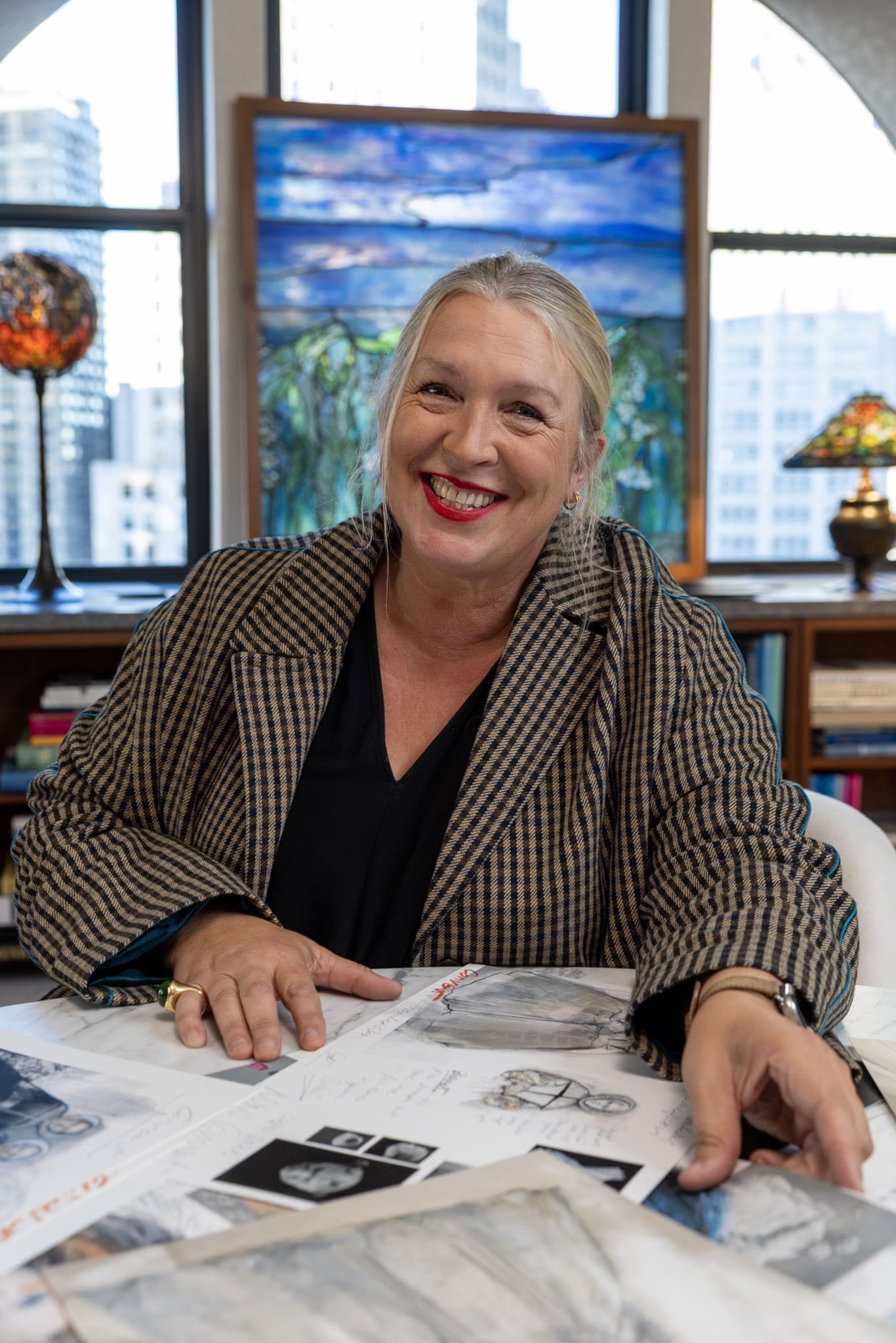 RIOT, NYC Creative Agency: Kate Hawley smiling with costume sketches and design references on table Kate Hawley smiling with costume sketches and design references on table