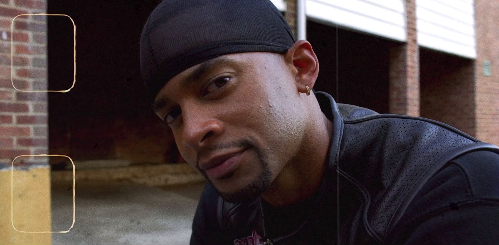 RIOT, NYC Creative Agency: Close-up of Mike Press wearing a black durag and leather jacket, exuding confidence in an urban setting. Close-up of Mike Press wearing a black durag and leather jacket, exuding confidence in an urban setting.