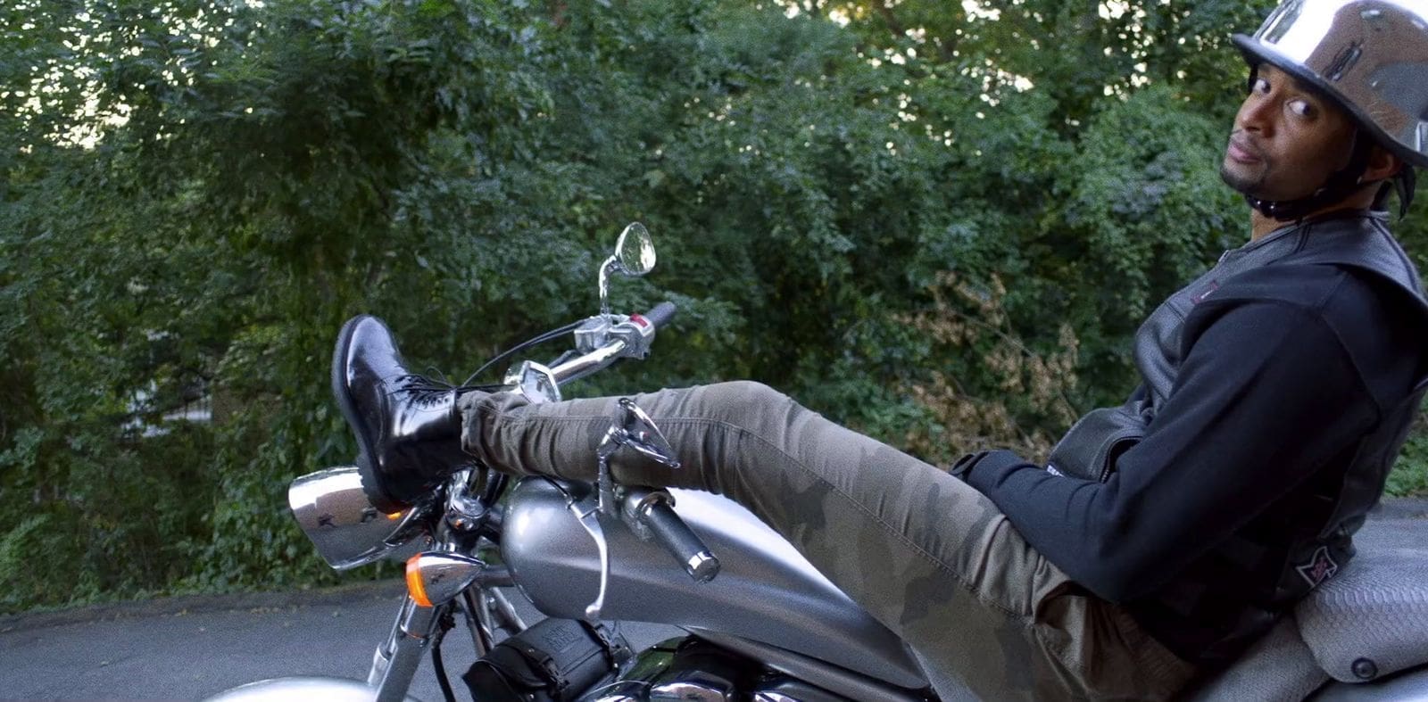 RIOT, NYC Creative Agency: Mike Press relaxing on a motorcycle in camo pants and a reflective helmet, surrounded by greenery. Mike Press relaxing on a motorcycle in camo pants and a reflective helmet, surrounded by greenery.