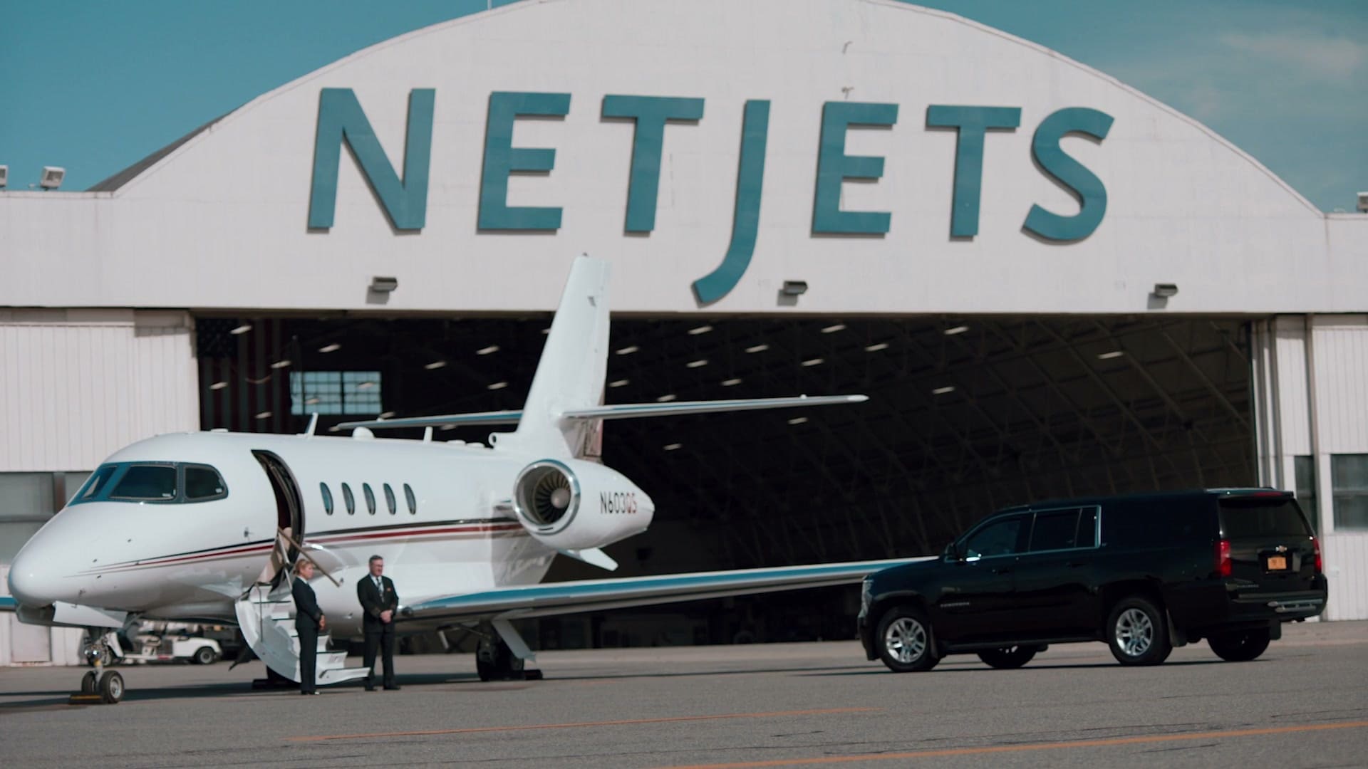 A NetJets jet and black SUV planeside outside the NetJets hangar at Westchester County Airport